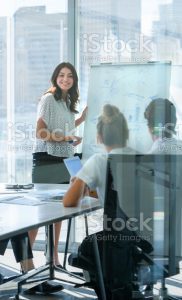 Woman giving a presentation to her team. She is using a whiteboard with charts and graphs.